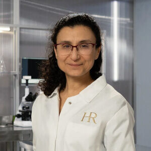 Scientifique en blouse blanche, souriant devant des equipements de laboratoire moderne.