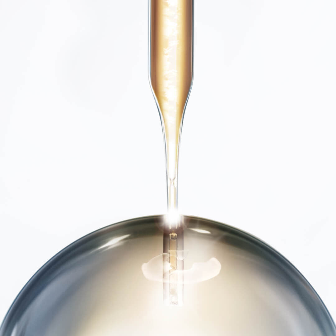 Une pipette deverse un liquide dore dans un receptacle, creant un effet de brillance et de profondeur.