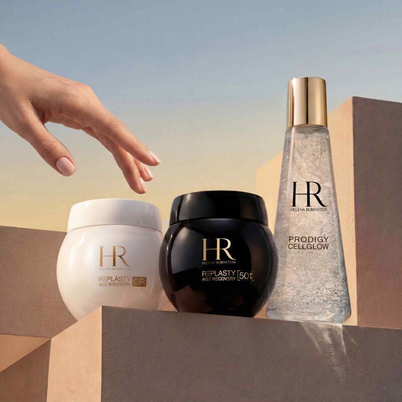 Flacon de serum Prodigy Cellglow (clair, bulles) et pot de creme Re-Plasty (noir) Helena Rubinstein. Poses sur un fond blanc texture et lumineux, symbolisant l'elegance et l'efficacite des soins.