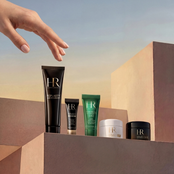 Une main tendue vers un flacon de produits de soin pour la peau posé sur une surface en bois.